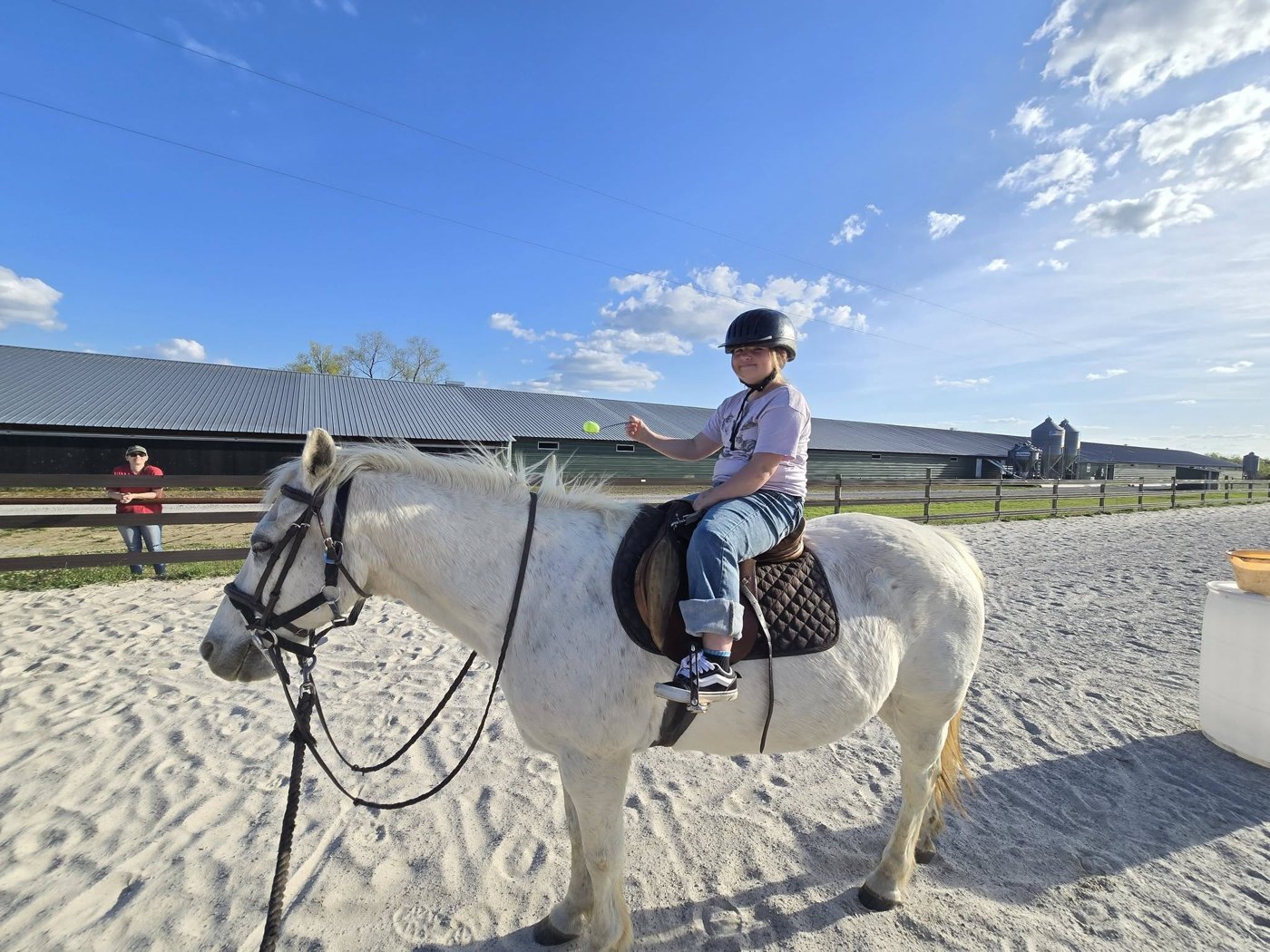 A young rider smiling atop a gentle white horse in the sunshine.